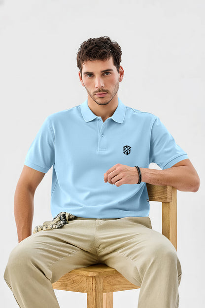Man wearing a light blue polo shirt with logo, beige pants, seated on wooden chair