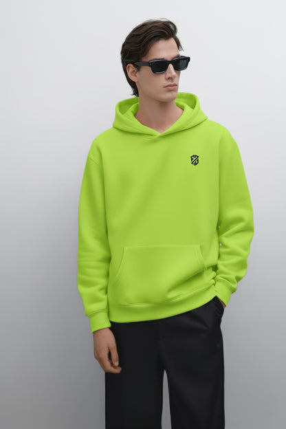 Man in neon green hoodie with chest logo, black pants, and sunglasses against plain background
