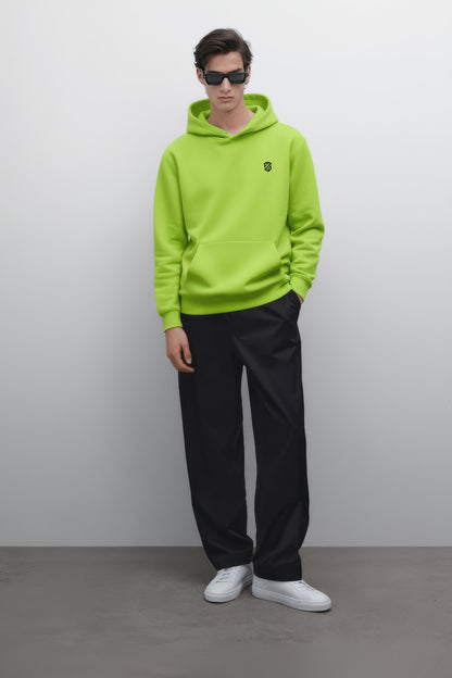 Man in neon green hoodie with chest logo, black pants, white sneakers, and sunglasses