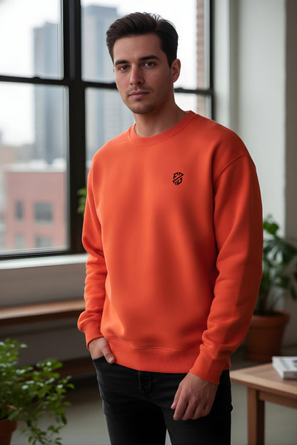 Man in modern orange sweatshirt with black logo, standing indoors by window