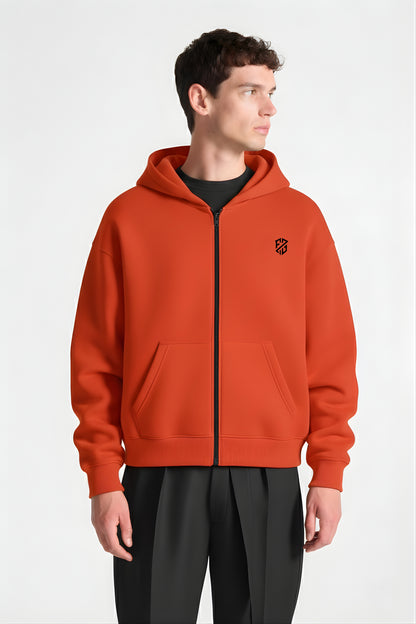 Man wearing orange zip-up hoodie with front pockets and black geometric logo, white background