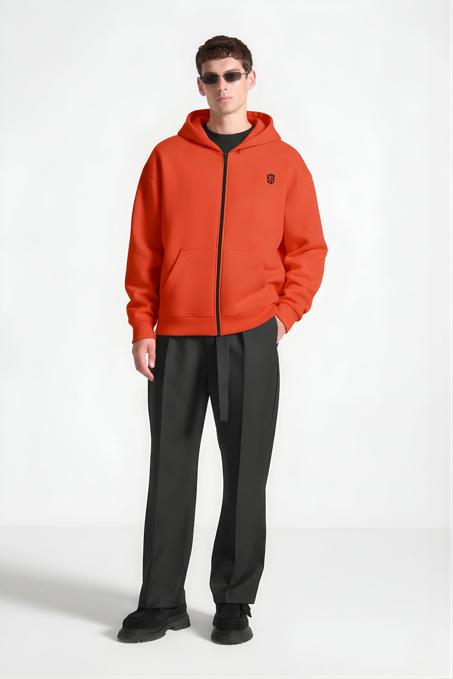 Man wearing orange zip-up hoodie with black logo, black trousers, and sunglasses
