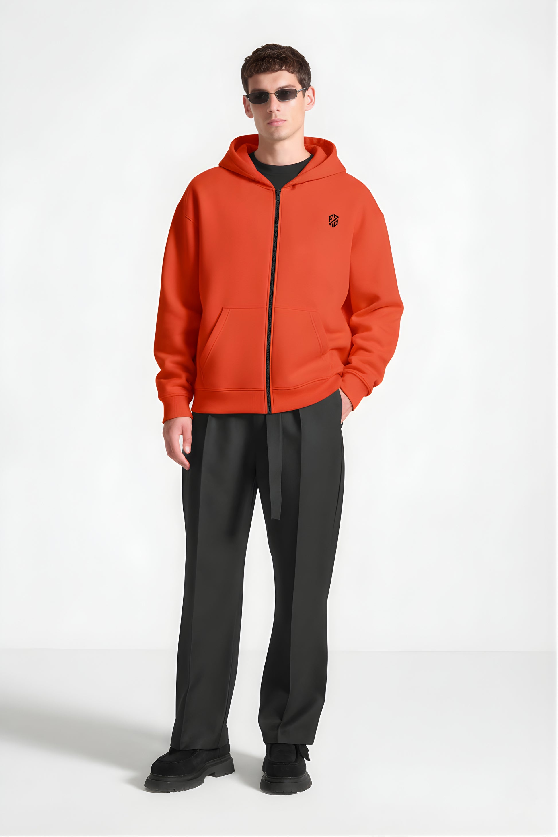 Man wearing orange zip-up hoodie with black logo, black trousers, and sunglasses
