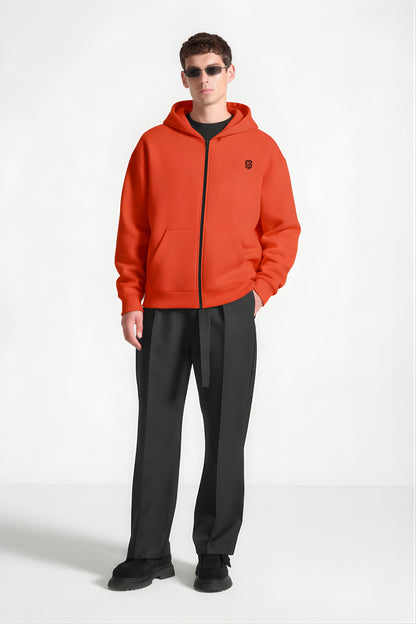 Man wearing orange zip-up hoodie with black logo, black trousers, and sunglasses