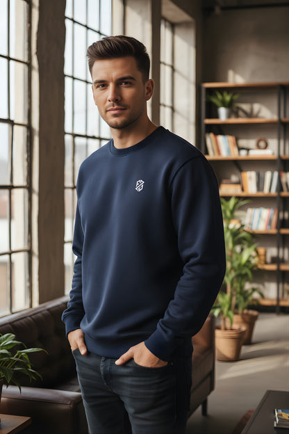Man in navy blue crewneck sweatshirt with logo, standing in modern living room
