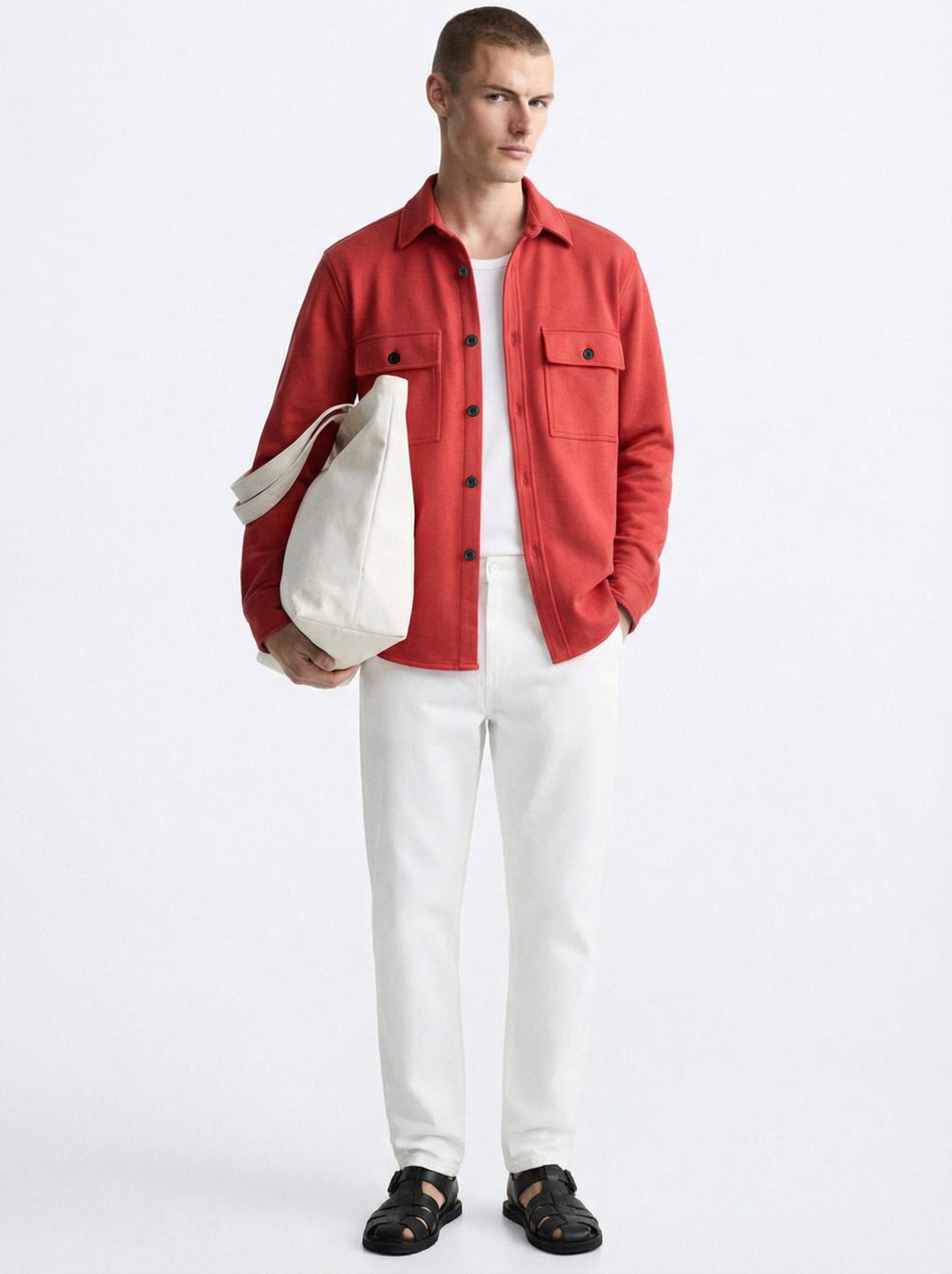 Man in a red overshirt, white pants, white tote bag, and black sandals on white background