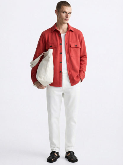 Man in a red overshirt, white pants, white tote bag, and black sandals on white background