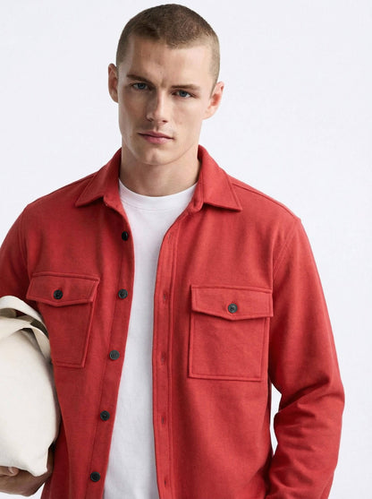 Man in red button-up shirt with flap pockets over white t-shirt, holding beige tote bag