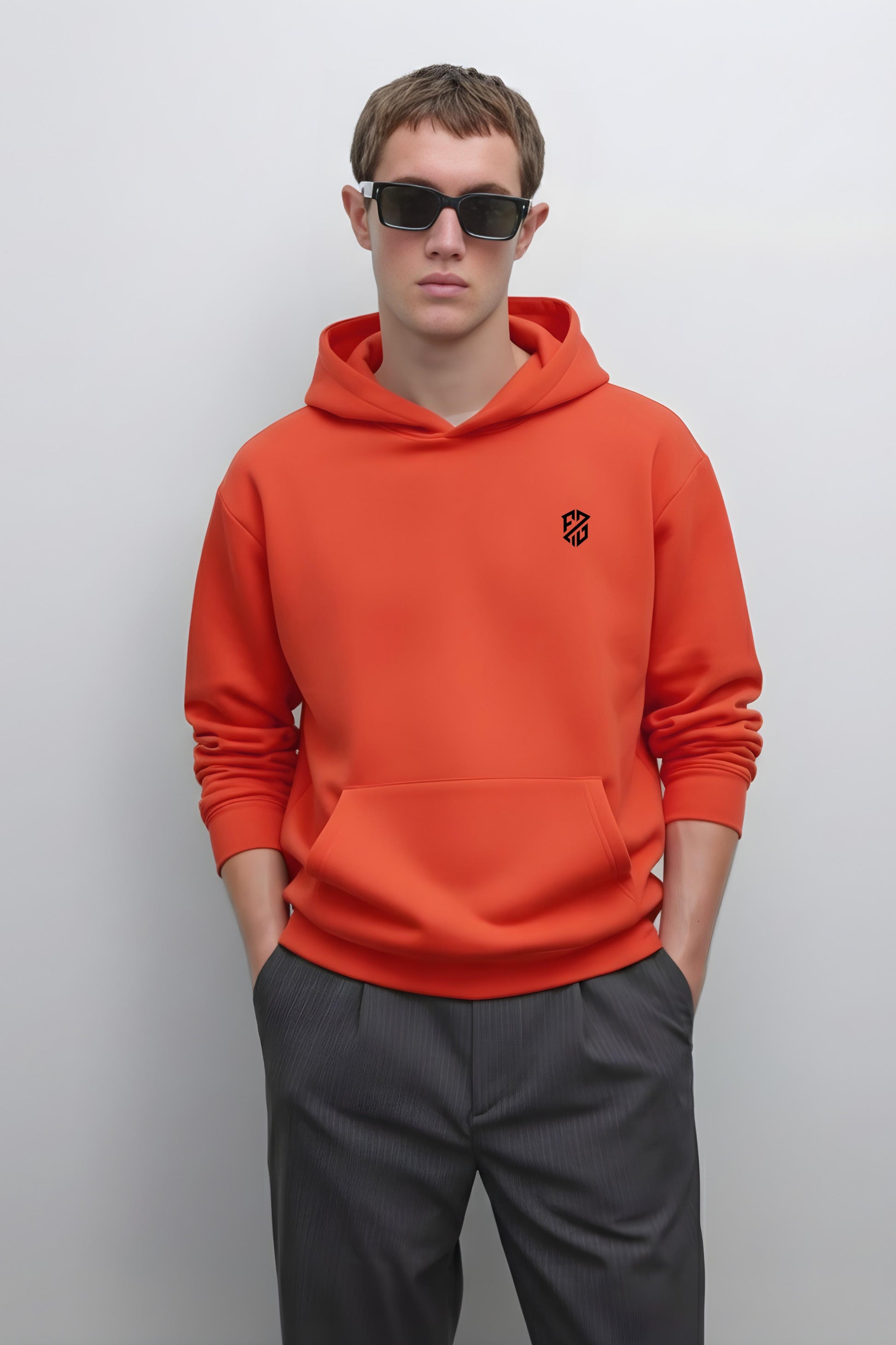 Man in orange hoodie with black chest logo and dark sunglasses, standing against white background