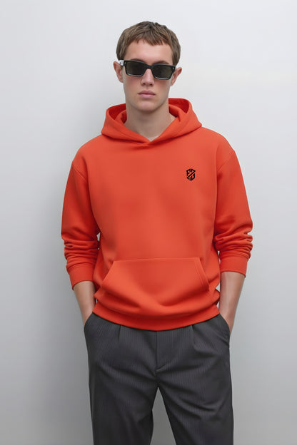 Man in orange hoodie with black chest logo and dark sunglasses, standing against white background