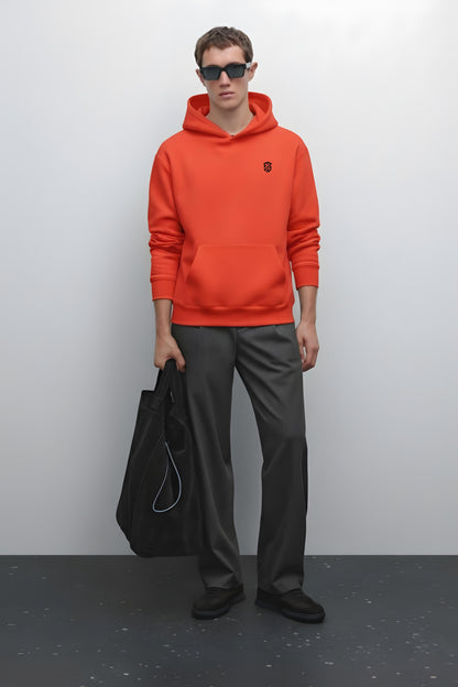 Man in orange hoodie with logo, black trousers, sunglasses, and holding a black tote bag