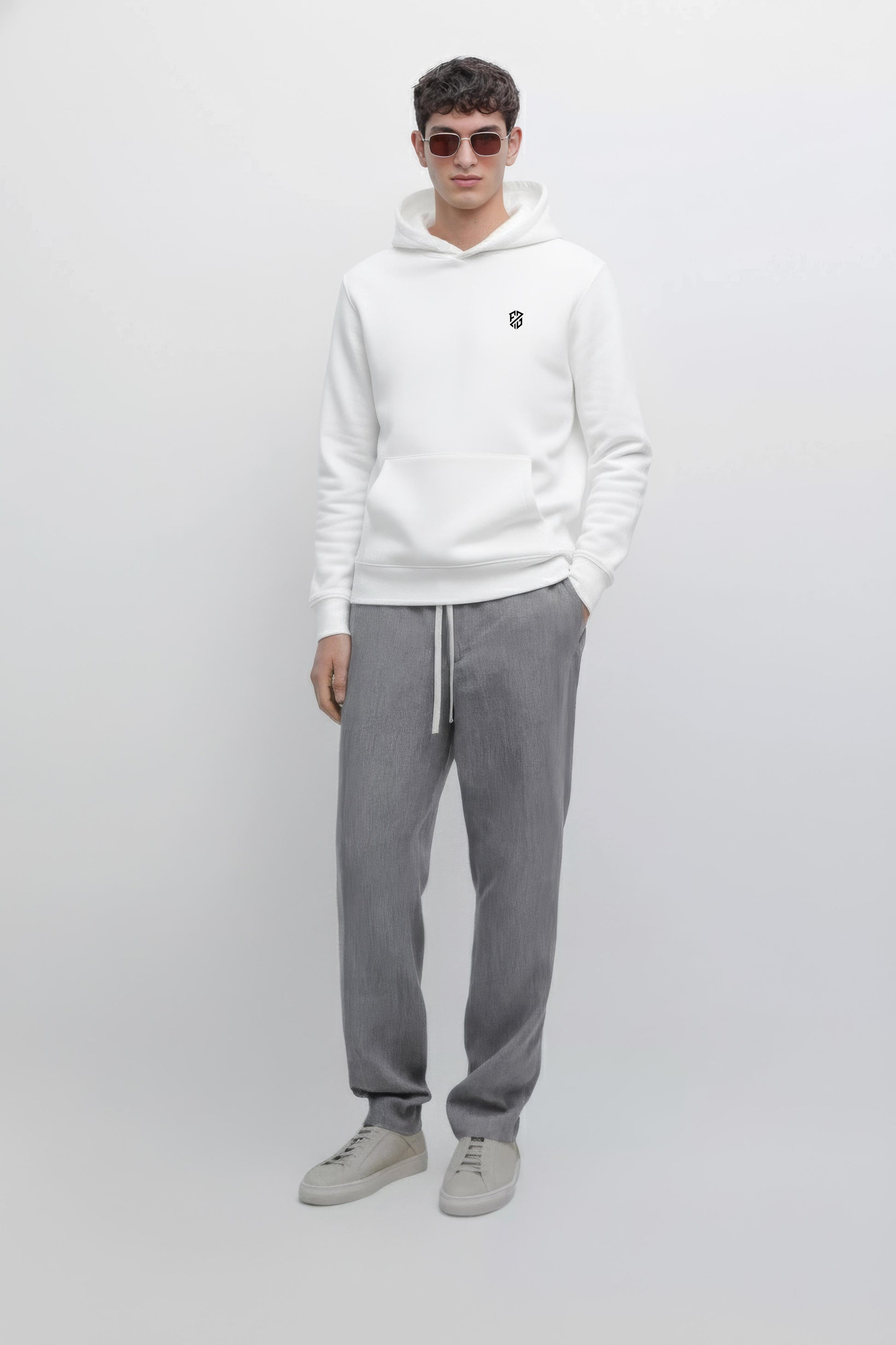Man in white hoodie with small chest logo, gray drawstring pants, and light gray sneakers