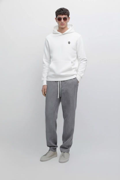 Man in white hoodie with small chest logo, gray drawstring pants, and light gray sneakers