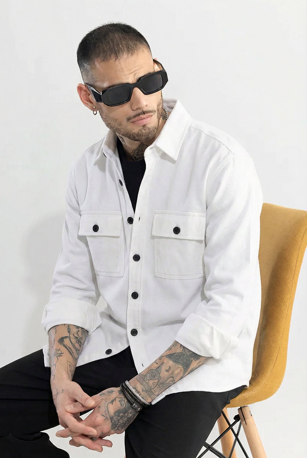 Man wearing a white button-up shirt with black buttons, sunglasses, and visible tattoos