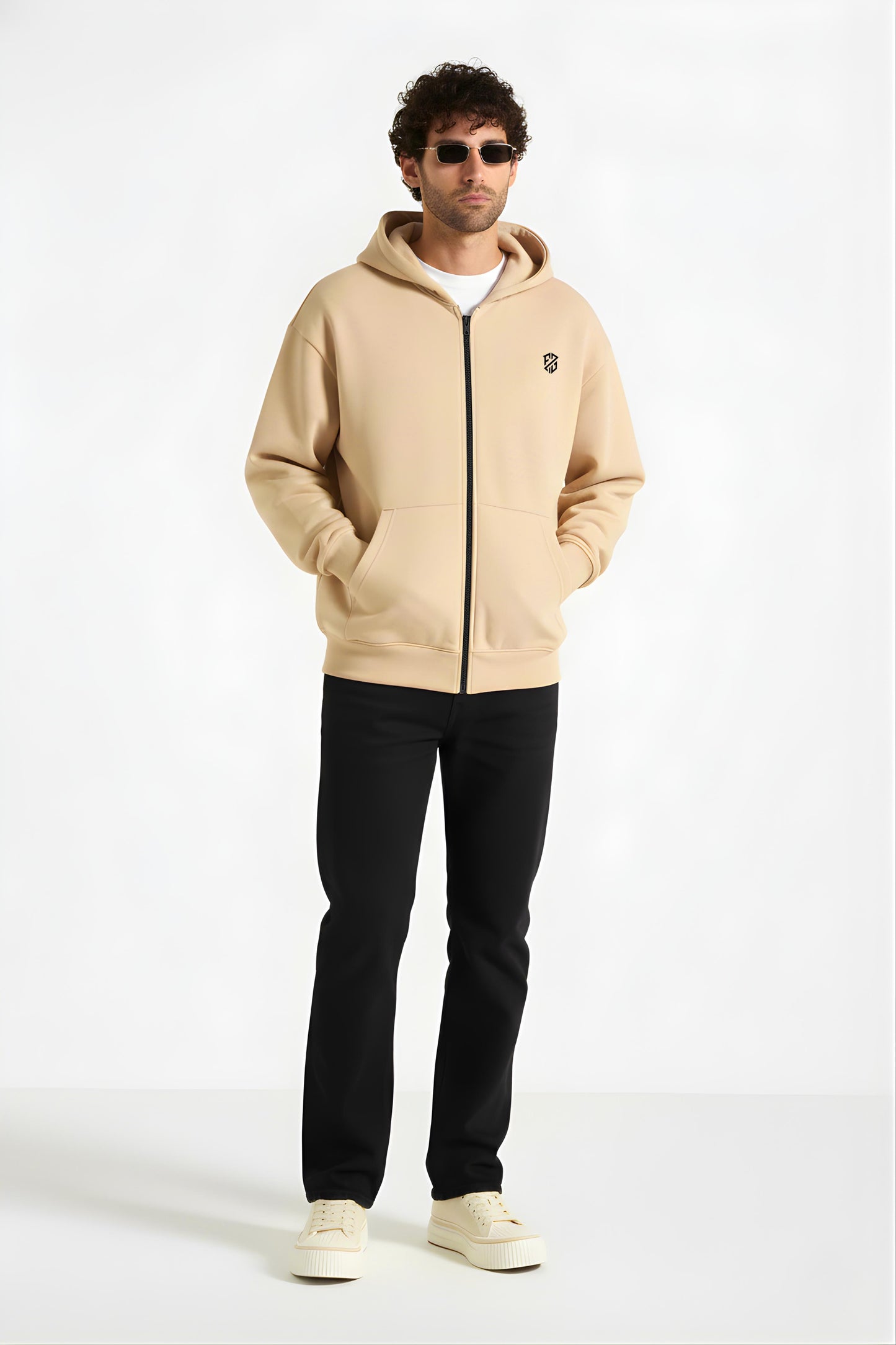 Man wearing beige zip-up hoodie with black pants and sneakers, casual streetwear fashion.