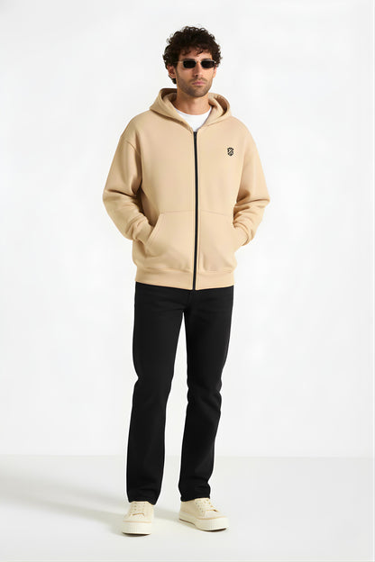 Man wearing beige zip-up hoodie with black pants and sneakers, casual streetwear fashion.