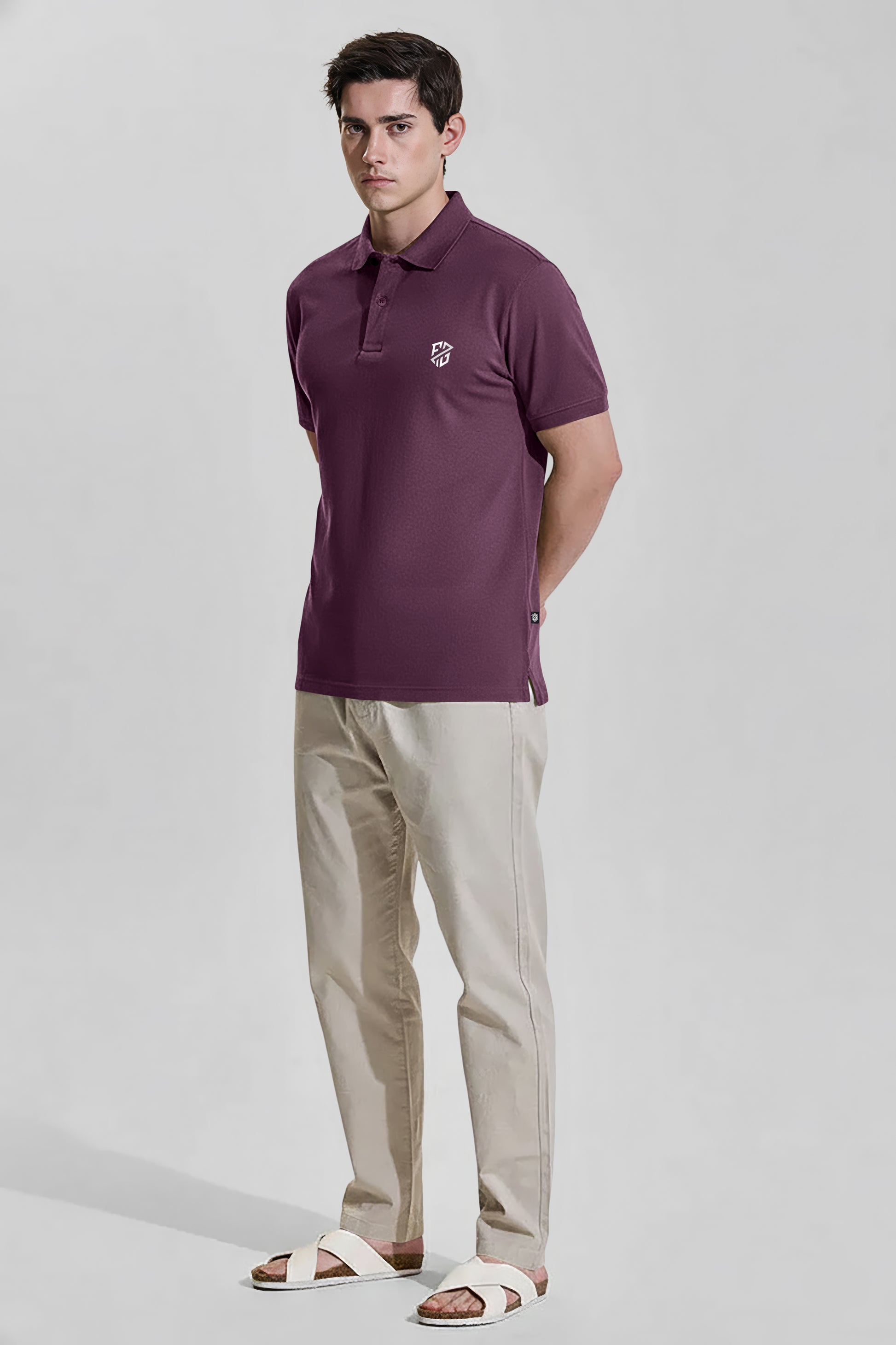 Man wearing burgundy polo shirt, beige pants, and white sandals on light background