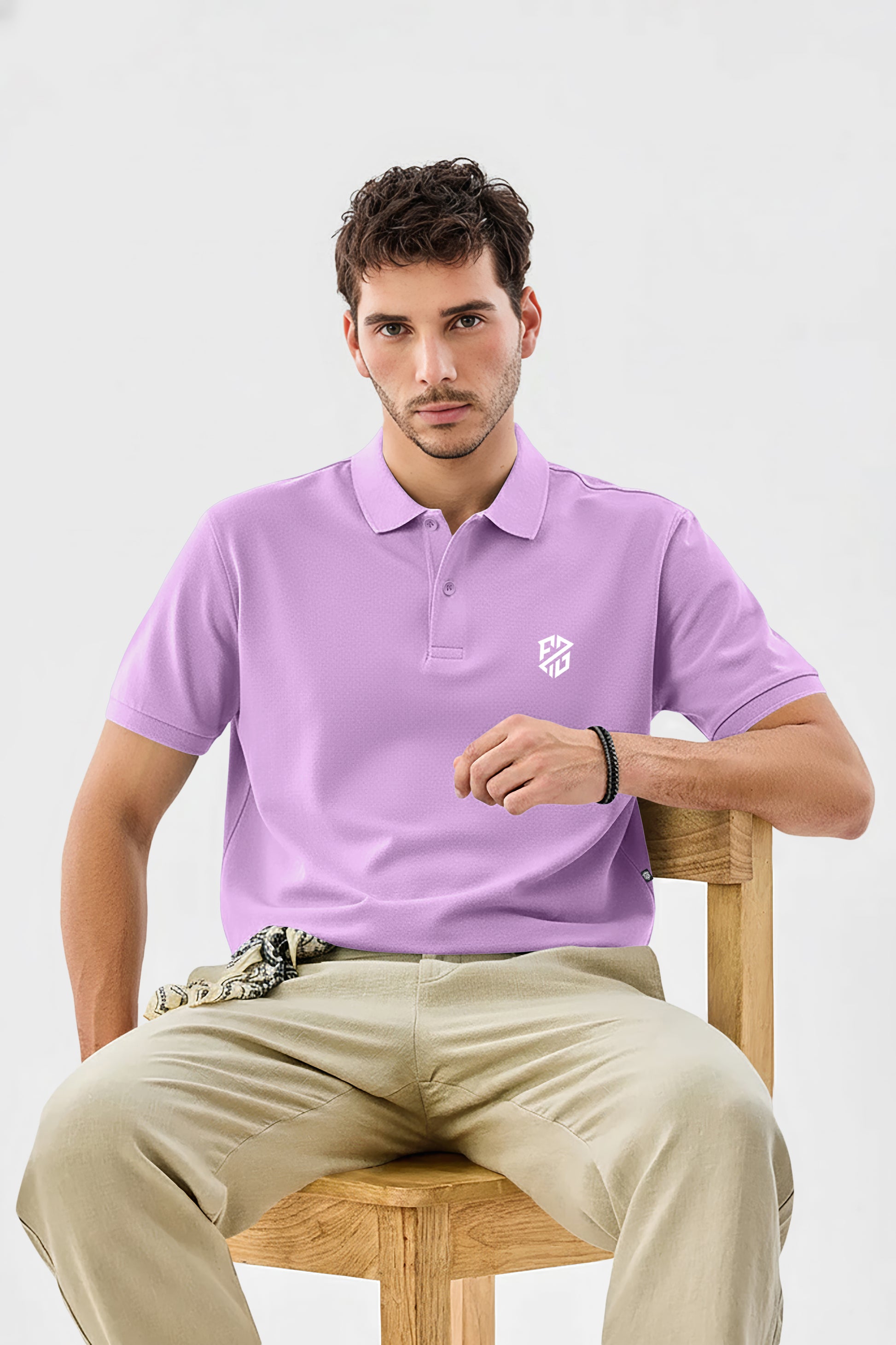 Man wearing a lavender short-sleeve polo shirt with white logo, beige pants, sitting on chair