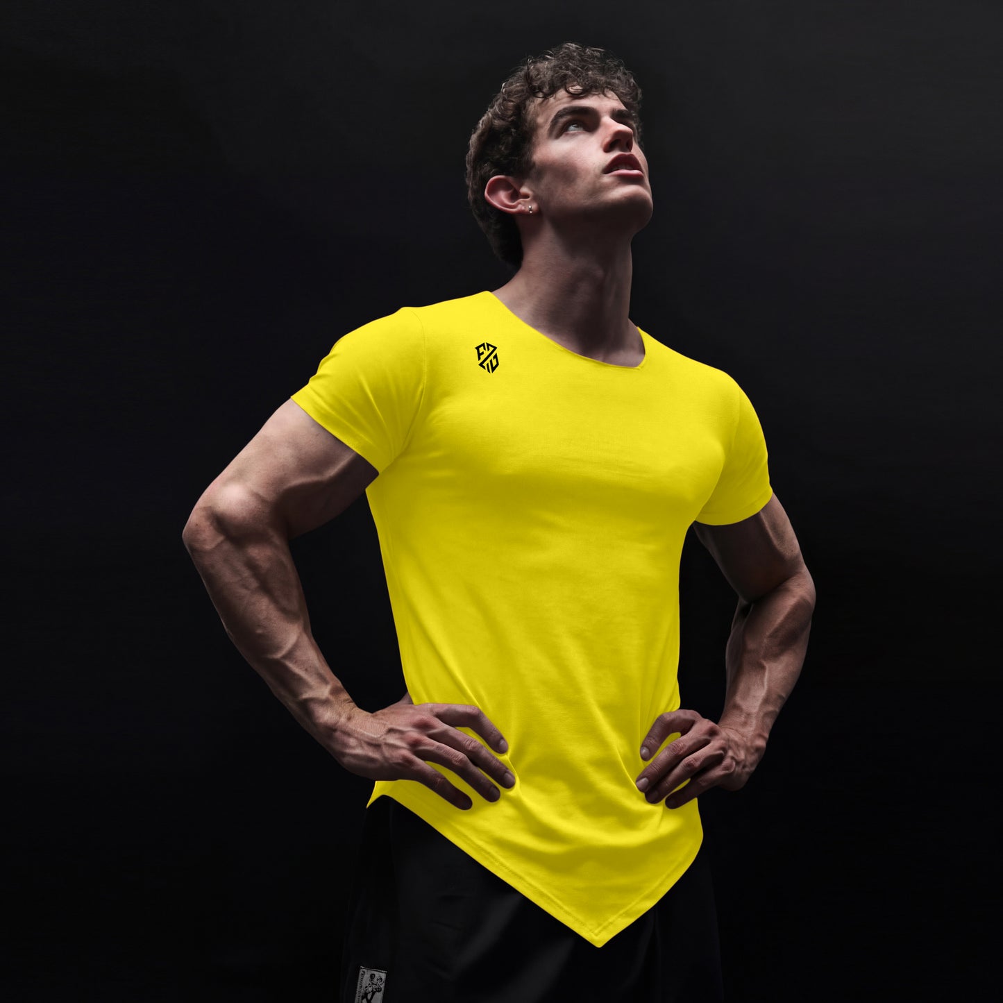 Man wearing bright yellow athletic t-shirt with angled hem, logo on shoulder, black background