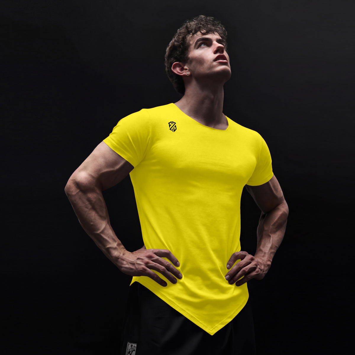Man wearing bright yellow athletic t-shirt with angled hem, logo on shoulder, black background