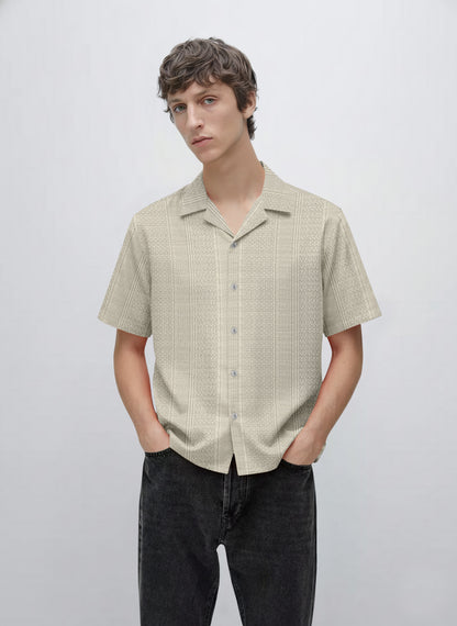 Man wearing a beige short sleeve button-up patterned shirt with black jeans