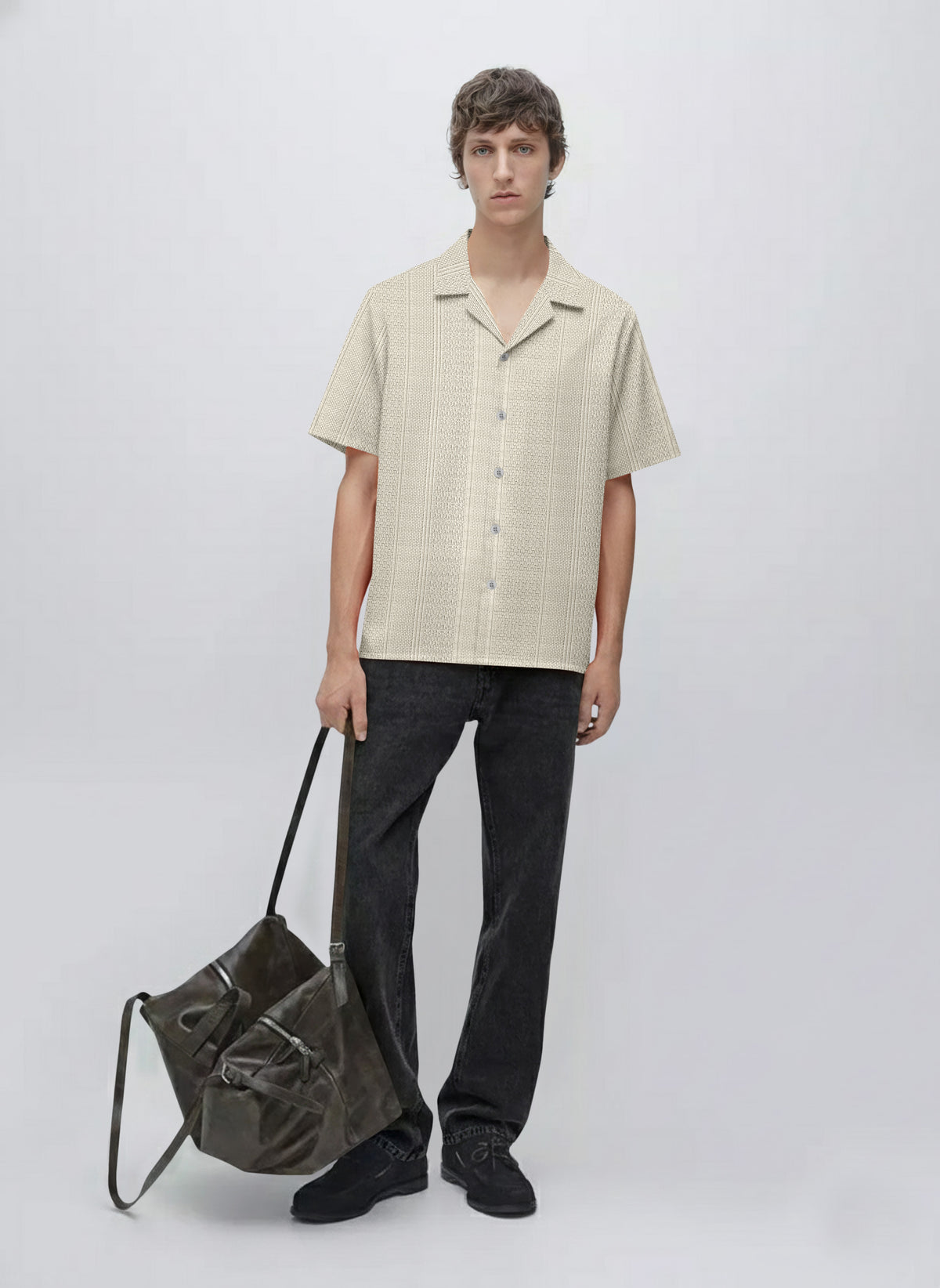 Man wearing a short sleeve beige button-up shirt, black jeans, and holding a large dark bag.