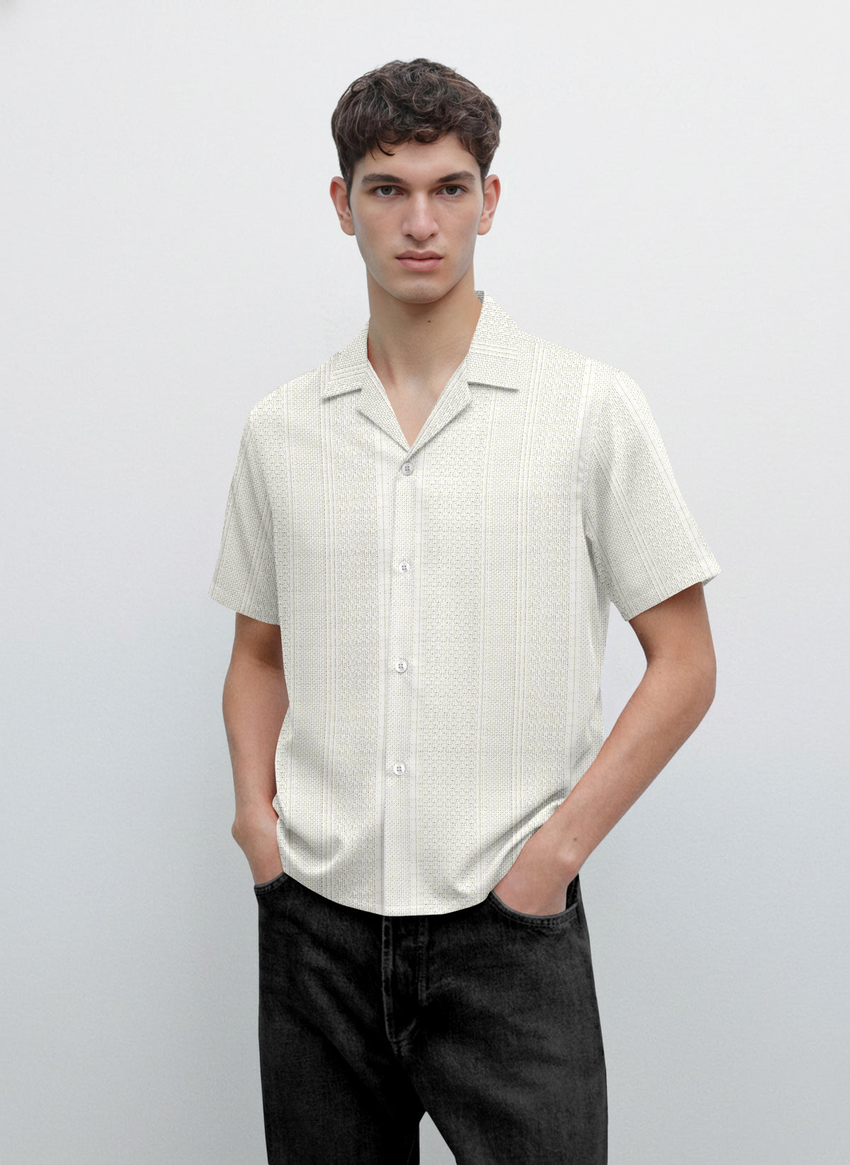 Man wearing short sleeve button-up cream patterned shirt and black jeans, minimalist background
