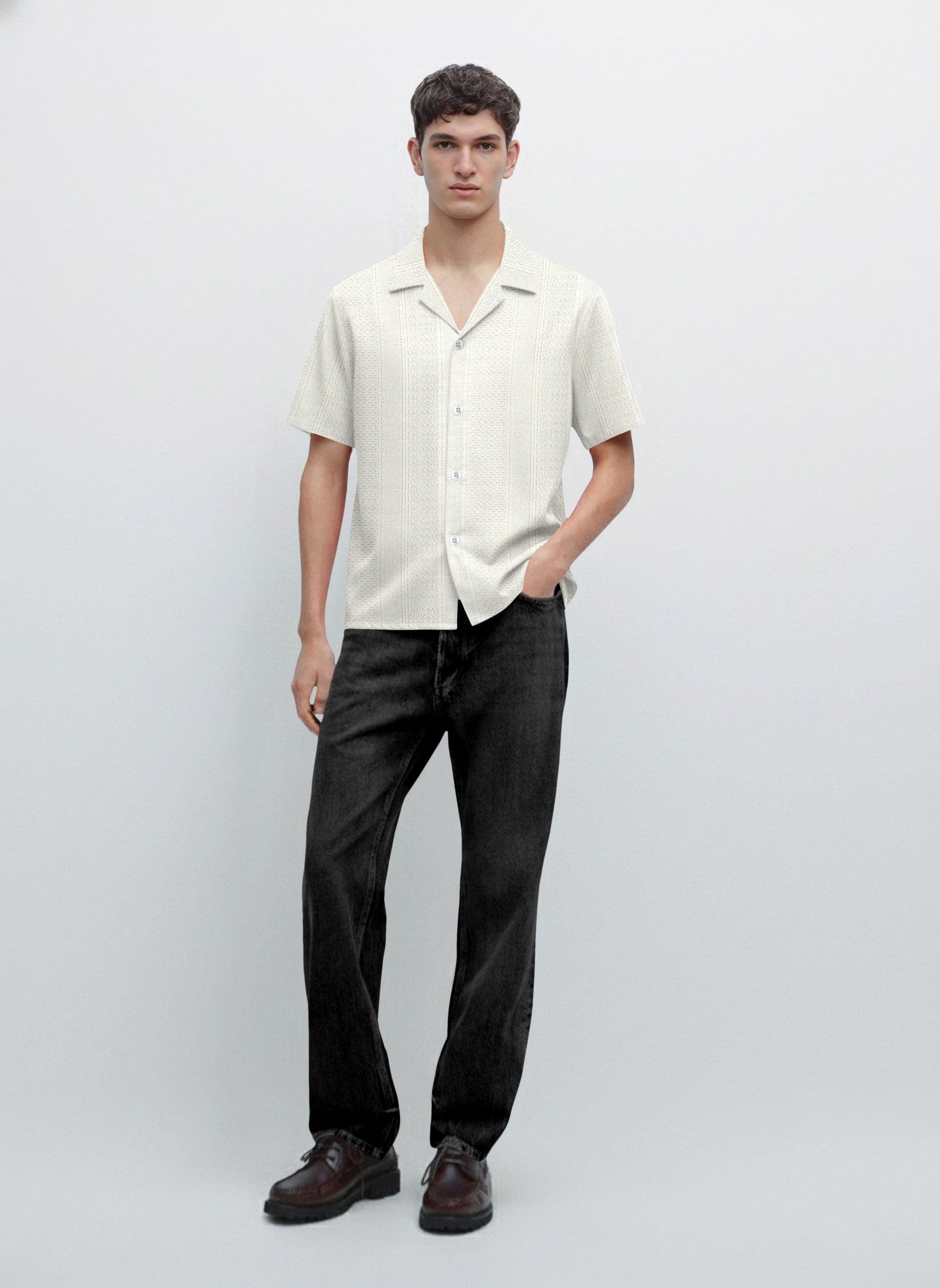 Man wearing a short sleeve white button-up shirt, black jeans, and brown shoes