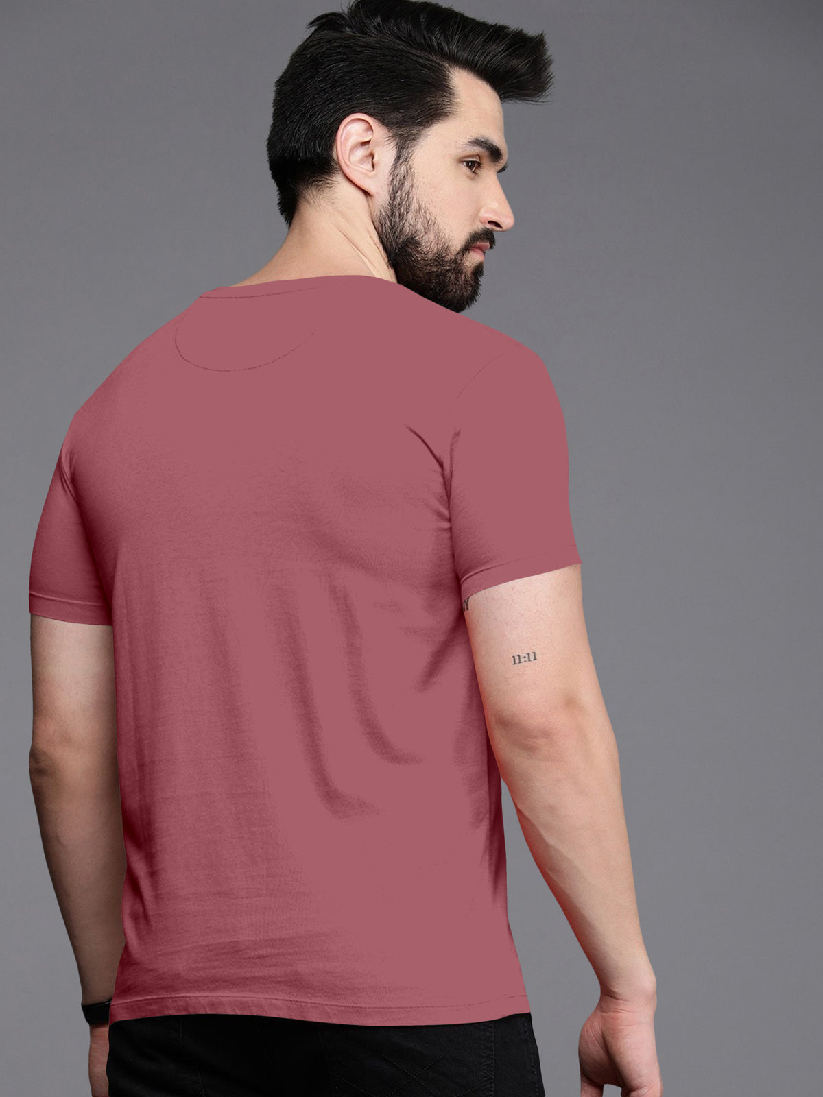 Man wearing plain mauve short sleeve t-shirt, viewed from the back, with 11:11 tattoo on arm.