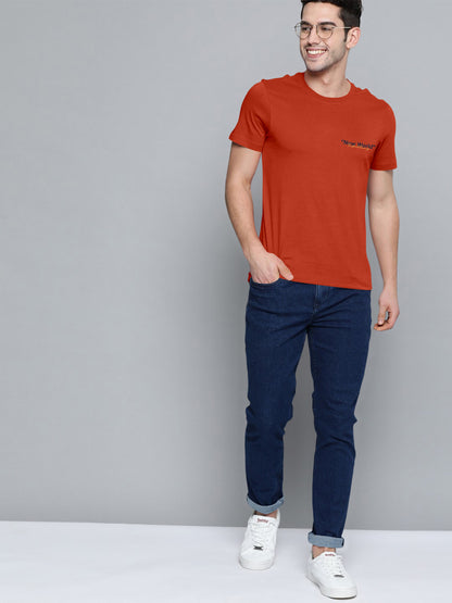 Man in orange graphic t-shirt with 'New World' text, blue jeans, and white sneakers
