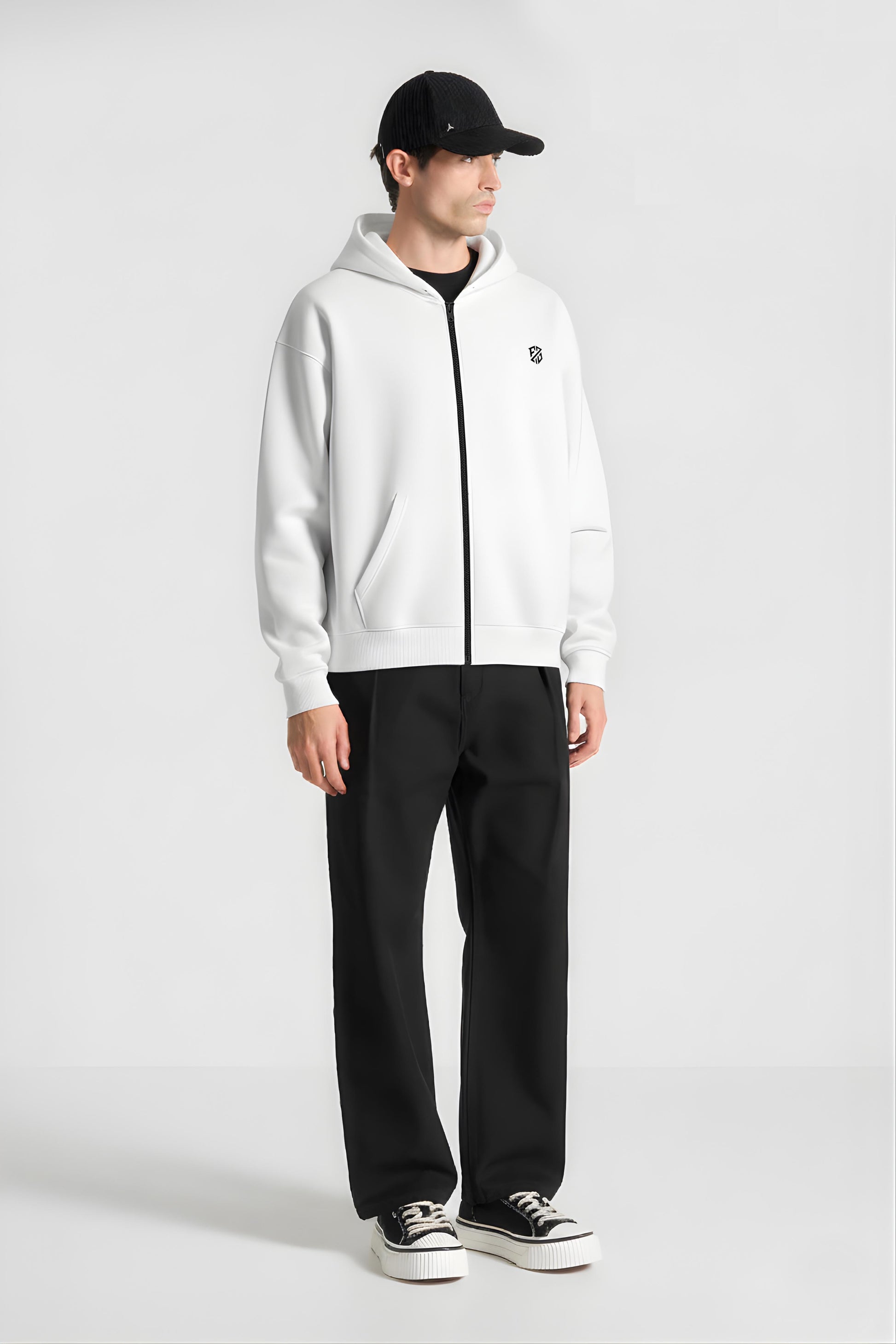Man in white zip up hoodie, black pants, black cap, and platform sneakers on white background