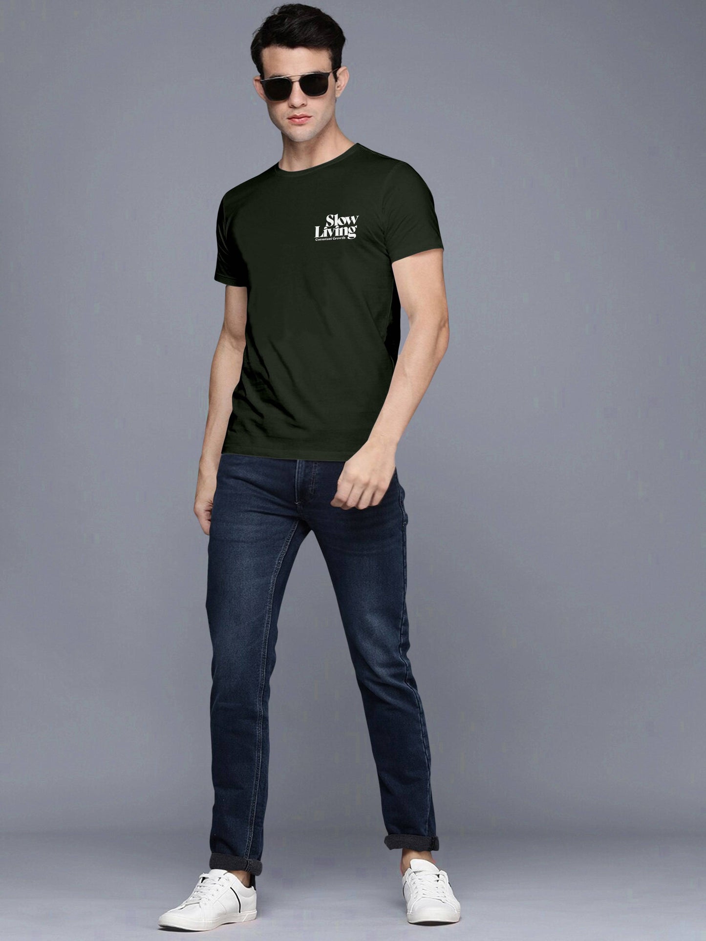 Man in black Slow Living t-shirt, blue jeans, white sneakers, and sunglasses posing