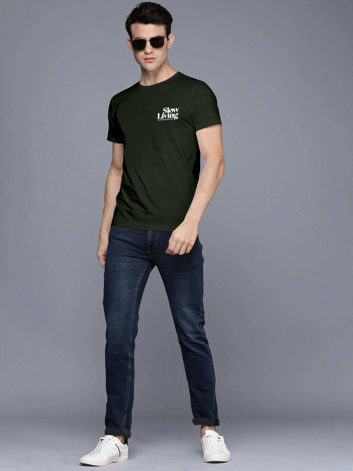 Man in black Slow Living t-shirt, blue jeans, white sneakers, and sunglasses posing